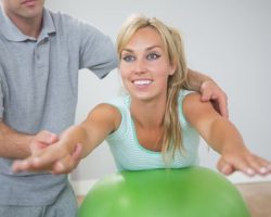 Physiotherapist correcting patient doing exercise on exercise ball - pelvic foor rehabilitation